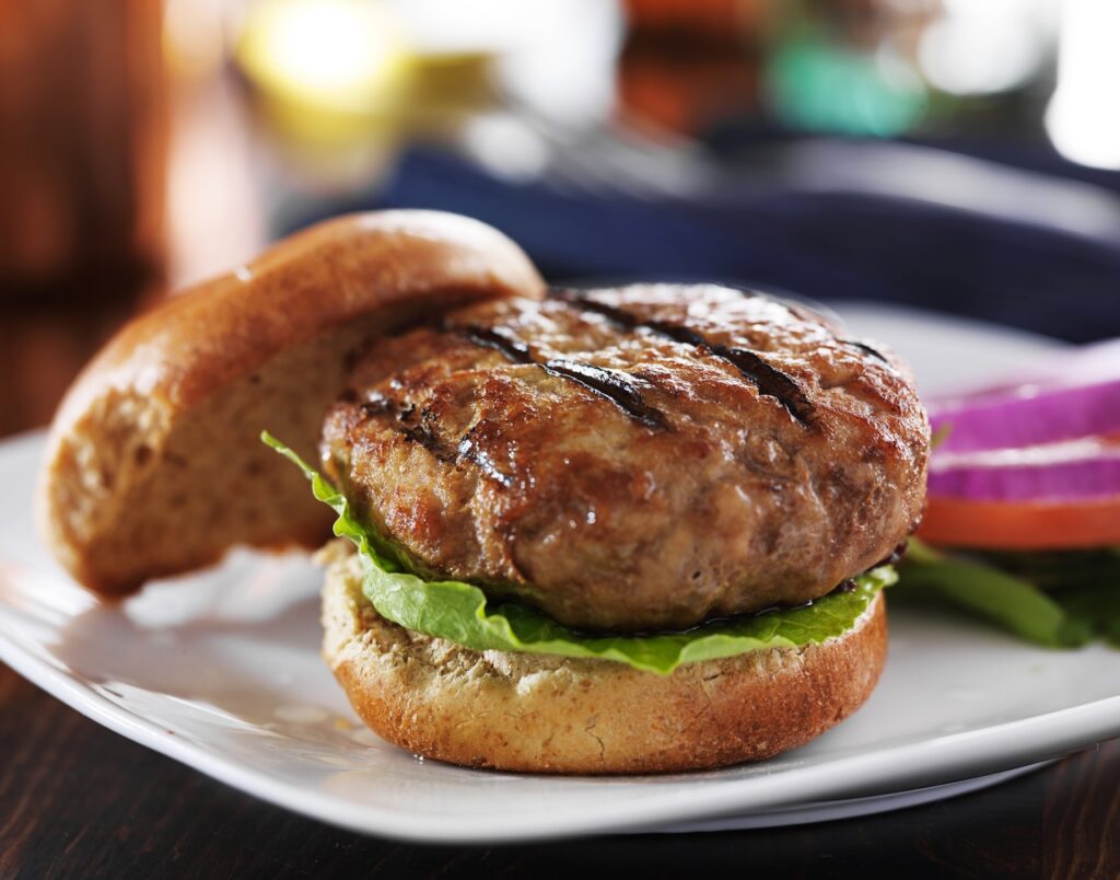 a burger on a plate with the top bun off to the side